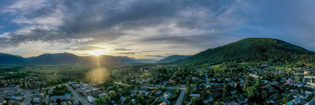 A sweeping aerial view of a small town at sunrise, with the sun peering over the mountains and casting a warm glow over the landscape.